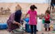 A woman and children gather water in a desert area of Gaza, highlighting daily life.