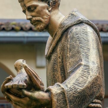 Bronze statue of a friar gently holding a dove, symbolizing peace and faith.