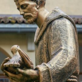Bronze statue of a friar gently holding a dove, symbolizing peace and faith.