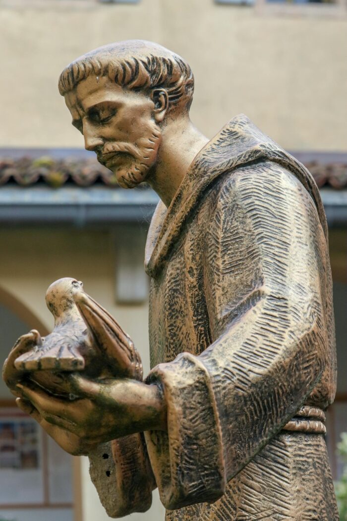 Bronze statue of a friar gently holding a dove, symbolizing peace and faith.